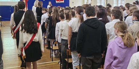Powiększ grafikę: Uczniowie i nauczyciele zebrani w sali gimnastycznej podczas apelu. Wejście pocztu sztandarowego.