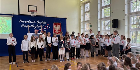 Powiększ grafikę: Zbiorowe zdjęcie uczniów prezentujących program artystyczny i nauczycieli podczas apelu w sali gimnastycznej.