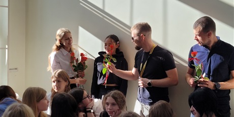 Powiększ grafikę: Uczniowie wręczają kwiaty nauczycielom w sali gimnastycznej.