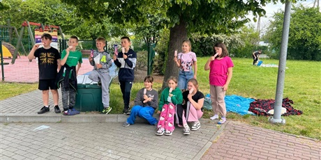 Powiększ grafikę: Uczniowie jedzą lody przy placu zabaw.