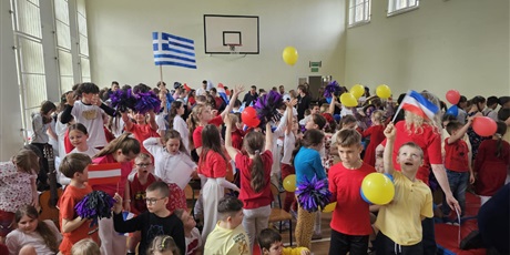 Powiększ grafikę: Uczniowie podczas wspólnego tańca z flagami i balonami w sali gimnastycznej.