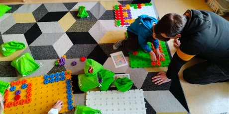 Powiększ grafikę: Dzieci w towarzystwie rodziców układają kompozycję z klocków w sali lekcyjnej.