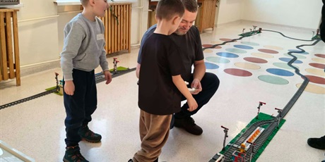 Powiększ grafikę: Uczniowie i instruktor podczas sterowania składem pociągu z klocków na korytarzu szkolnym.