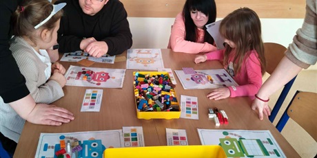 Powiększ grafikę: Dzieci w towarzystwie rodziców wykonują zadanie plastyczne w sali lekcyjnej.