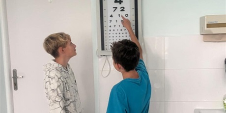 Powiększ grafikę: Uczniowie w gabinecie pani pielęgniarki przy tablicy do badania wzroku.