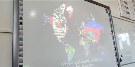 Powiększ grafikę: Prezentacja mapy Euroazji i Ameryk na ekranie w sali lekcyjnej.