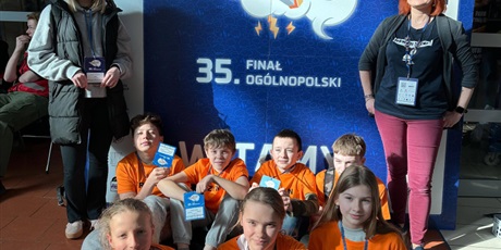 Powiększ grafikę: Uczestnicy konkursu i trenerki na tle banera konkursowego.