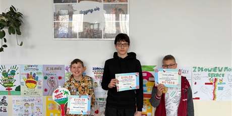 Powiększ grafikę: Uczniowie z dyplomami i nagrodami za konkurs na korytarzu szkolnym.
