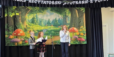 Powiększ grafikę: Pani dyrektor oraz uczniowie prowadzący konkurs na scenie.