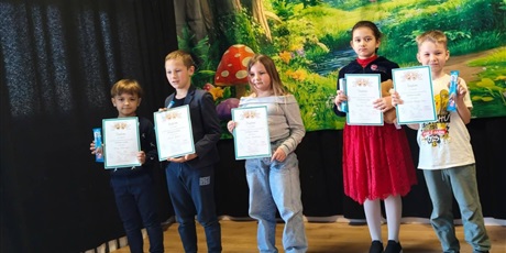 Powiększ grafikę: Zbiorowe zdjęcie uczestników konkursu z dyplomami i nagrodami na scenie.