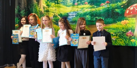 Powiększ grafikę: Zbiorowe zdjęcie uczestników konkursu z dyplomami i nagrodami na scenie.