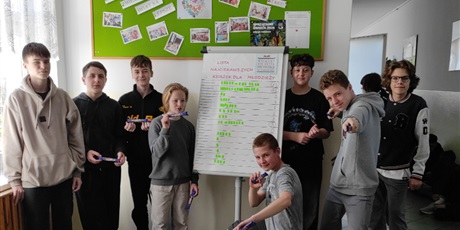 Powiększ grafikę: Uczniowie przy liście najciekawszych lektur na korytarzu szkolnym.