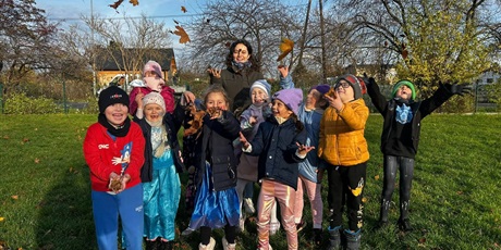 Powiększ grafikę: Uczniowie  w przebraniach  za postacie z bajek oraz nauczycielka przed szkołą podrzucają kolorowe liście.