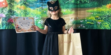 Powiększ grafikę: Uczestniczka konkursu w przebraniu z dyplomem i nagrodą na scenie.