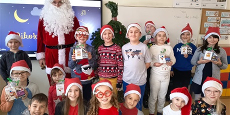 Powiększ grafikę: Zbiorowe zdjęcie uczniów w czapkach z Mikołajem w sali lekcyjnej.
