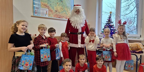 Powiększ grafikę: Zbiorowe zdjęcie uczniów z prezentami i Mikołajem w sali lekcyjnej.