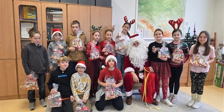 Powiększ grafikę: Zbiorowe zdjęcie uczniów z prezentami i Mikołajem w sali lekcyjnej.