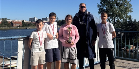 Powiększ grafikę: Zbiorowe zdjęcie uczniów i nauczyciela z medalami i pucharem na przystani wioślarskiej.