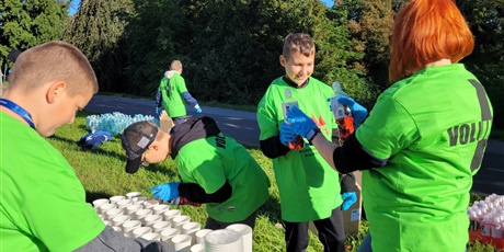 Powiększ grafikę: Uczniowie i nauczyciel podczas przygotowania napoi dla uczestników półmaratonu.