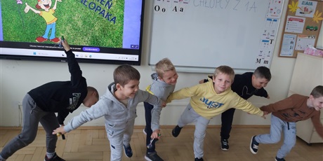 Powiększ grafikę: Uczniowie w sali lekcyjnej wykonują zadania sportowe.