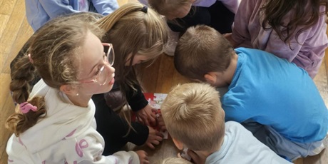 Powiększ grafikę: Uczniowie siedzą na podłodze w sali gimnastycznej, rozwiązują zadania.