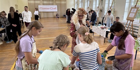 Powiększ grafikę: Uczniowie przygotowują zdrowe przekąski w sali gimnastycznej. Jurorzy przyglądają się ich pracy.