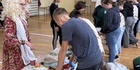 Powiększ grafikę: Uczniowie przygotowują zdrowe przekąski w sali gimnastycznej. Osoba z jury obserwuje ich pracę.