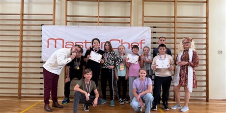 Powiększ grafikę: Zbiorowe zdjęcie uczestników konkursu kulinarnego z dyplomami i medalami z jurorami w sali gimnastycznej.