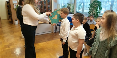 Powiększ grafikę: Dyrektor  i uczniowie podczas pasowania na czytelnika w bibliotece.