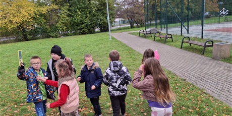 Powiększ grafikę: Uczniowie przy boisku szkolnym z kartą pracy.