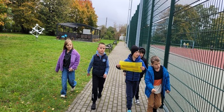 Powiększ grafikę: Uczniowie przy  boisku szkolnym z kartą pracy.