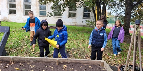 Powiększ grafikę: Uczniowie przy szkole z kartą pracy.
