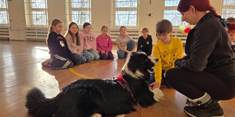 Powiększ grafikę: Uczniowie podczas zajęć z psim terapeutą w sali gimnastycznej.