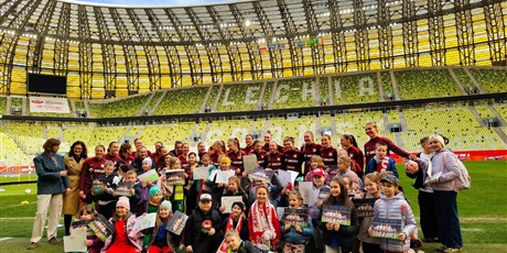 Powiększ grafikę: Zbiorowe zdjęcie uczestników spotkania z piłkarkami na stadionie.