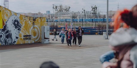 Powiększ grafikę: Nauczyciel i uczniowie w drodze na stadion piłkarski.