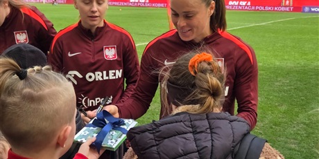 Powiększ grafikę: Uczniowie wręczają upominek reprezentantkom  Polski w piłce nożnej na stadionie.