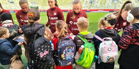 Powiększ grafikę: Uczniowie otrzymują autografy reprezentantek Polski w piłce nożnej na stadionie.