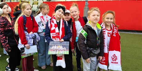 Powiększ grafikę: Uczniowie z szalikami w barwach narodowych na stadionie piłkarskim.