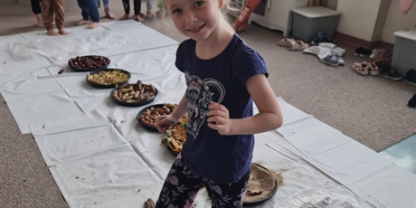 Powiększ grafikę: Na podłodze misy z różnymi nasionami ustawione w jednej linii. Uczennica pokonuje "ścieżkę sensoryczną".