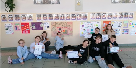 Powiększ grafikę: Zbiorowe zdjęcie uczniów pod napisem "Dzień Tabliczki Mnożenia" na korytarzu szkolnym.