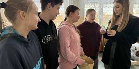 Powiększ grafikę: Uczniowie i nauczyciel losują i odpowiadają na zadania matematyczne w sali lekcyjnej.