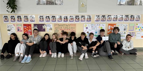 Powiększ grafikę: Zbiorowe zdjęcie uczniów pod napisem "Dzień Tabliczki Mnożenia" na korytarzu szkolnym.