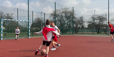 Powiększ grafikę: Uczniowie podczas gry w piłkę nożną na boisku szkolnym.