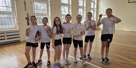 Powiększ grafikę: Zbiorowe zdjęcie uczennic z medalami i dyplomem w sali gimnastycznej.