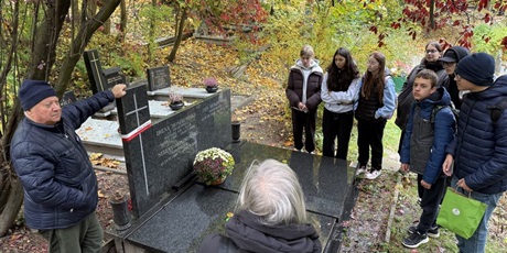 Powiększ grafikę: Uczniowie i starsze osoby  przy grobie na cmentarzu.