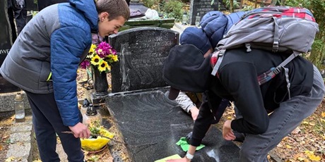 Powiększ grafikę: Uczniowie porządkują groby na cmentarzu.