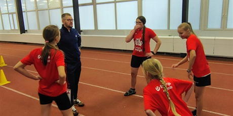 Powiększ grafikę: Uczniowie i nauczyciel podczas ćwiczeń ruchowych na hali sportowej.