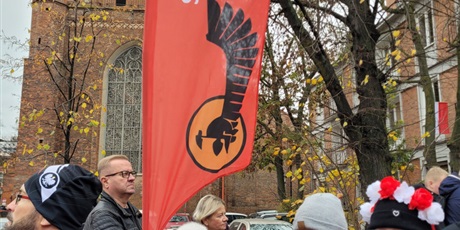 Powiększ grafikę: Uczniowie z flagami, symbolami narodowymi  i banerami szkolnymi na ulicy podczas parady niepodległości.