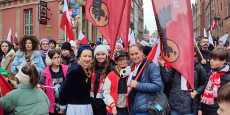 Powiększ grafikę: Uczniowie i nauczyciele  z flagami, symbolami narodowymi  i banerami szkolnymi na ulicy podczas parady niepodległości.