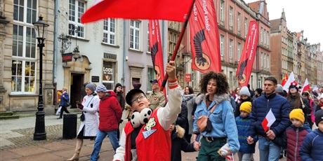 Powiększ grafikę: Uczniowie z flagami, symbolami narodowymi  i banerami szkolnymi na ulicy podczas parady niepodległości.